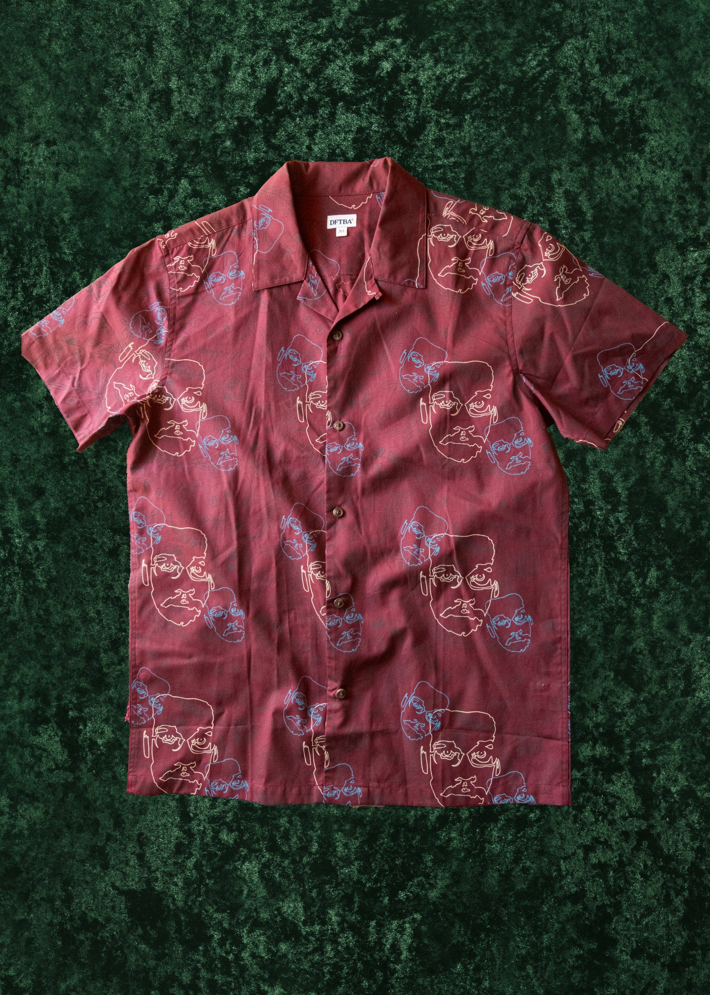 Maroon patterned button-up shirt with line art of Pizza John and ingredients on a textured green surface