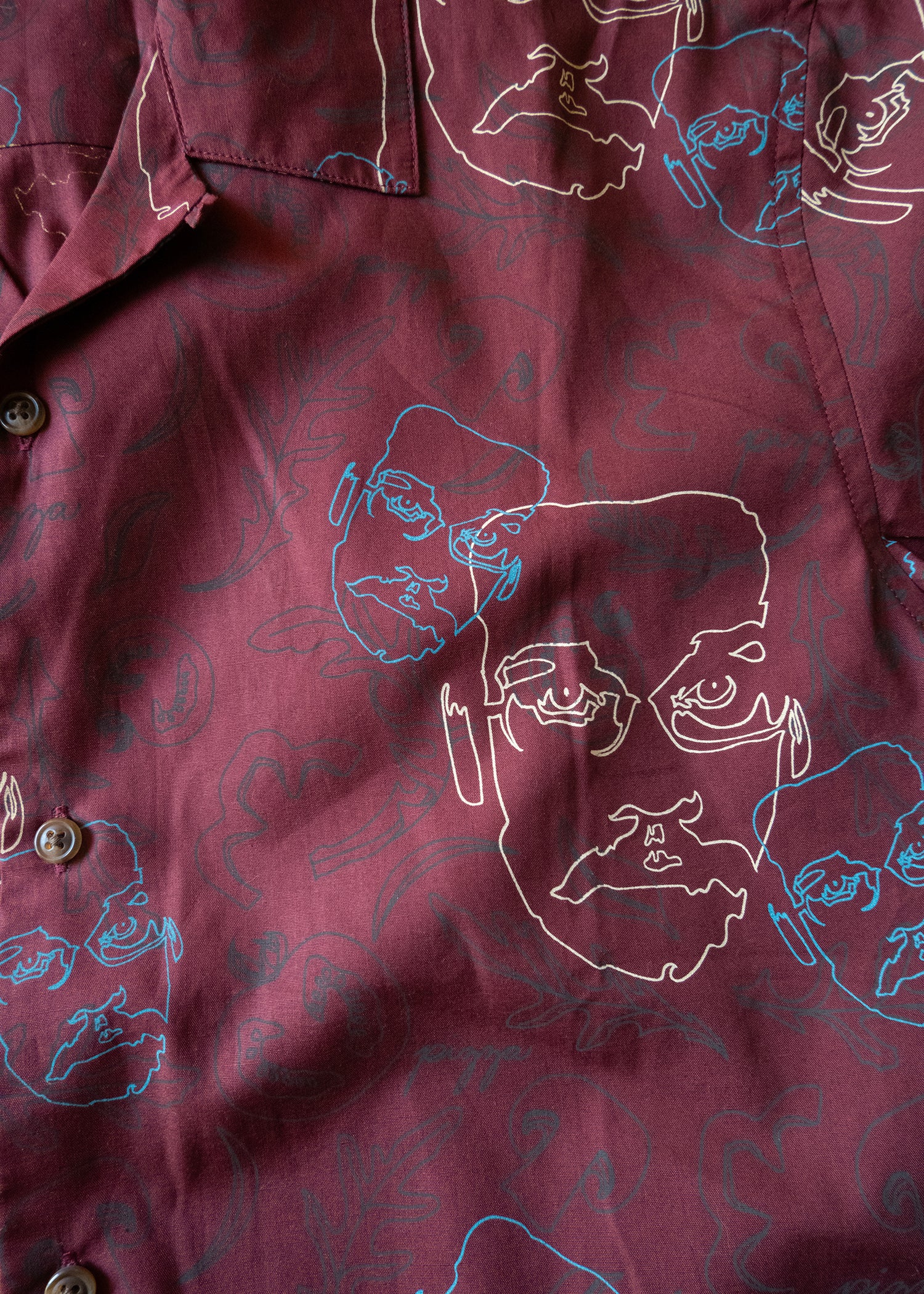 Maroon shirt with white and blue line art of Pizza John face and ingredients in gray behind them.