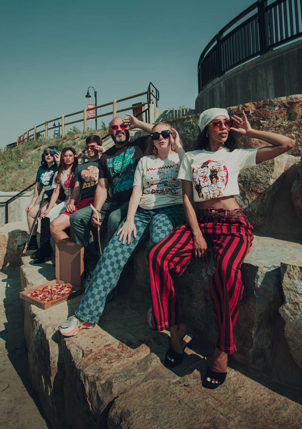 Group of people sitting on stone steps outdoors, wearing sunglasses and Pizzamas shirts.