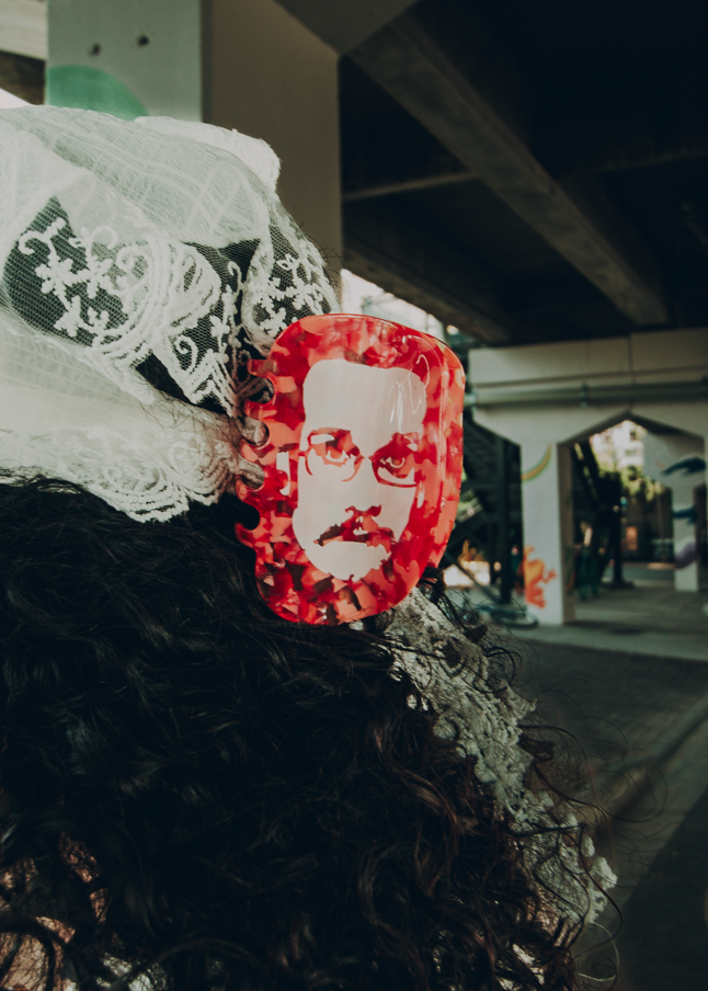 Person wearing a headscarf with a red hair clip with Pizza John's face in an urban setting