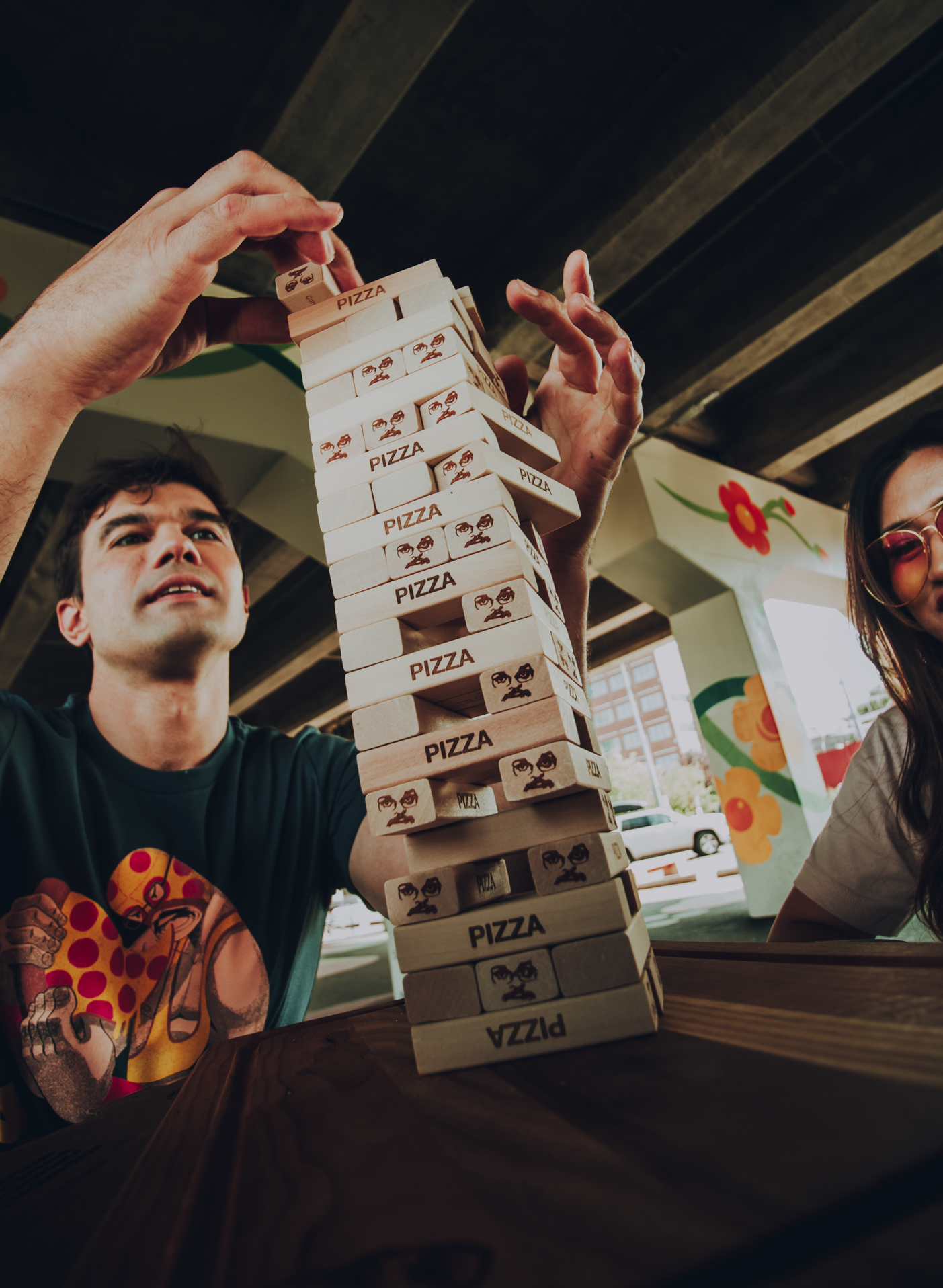 Two people playing with a tower of pizza-themed blocks.