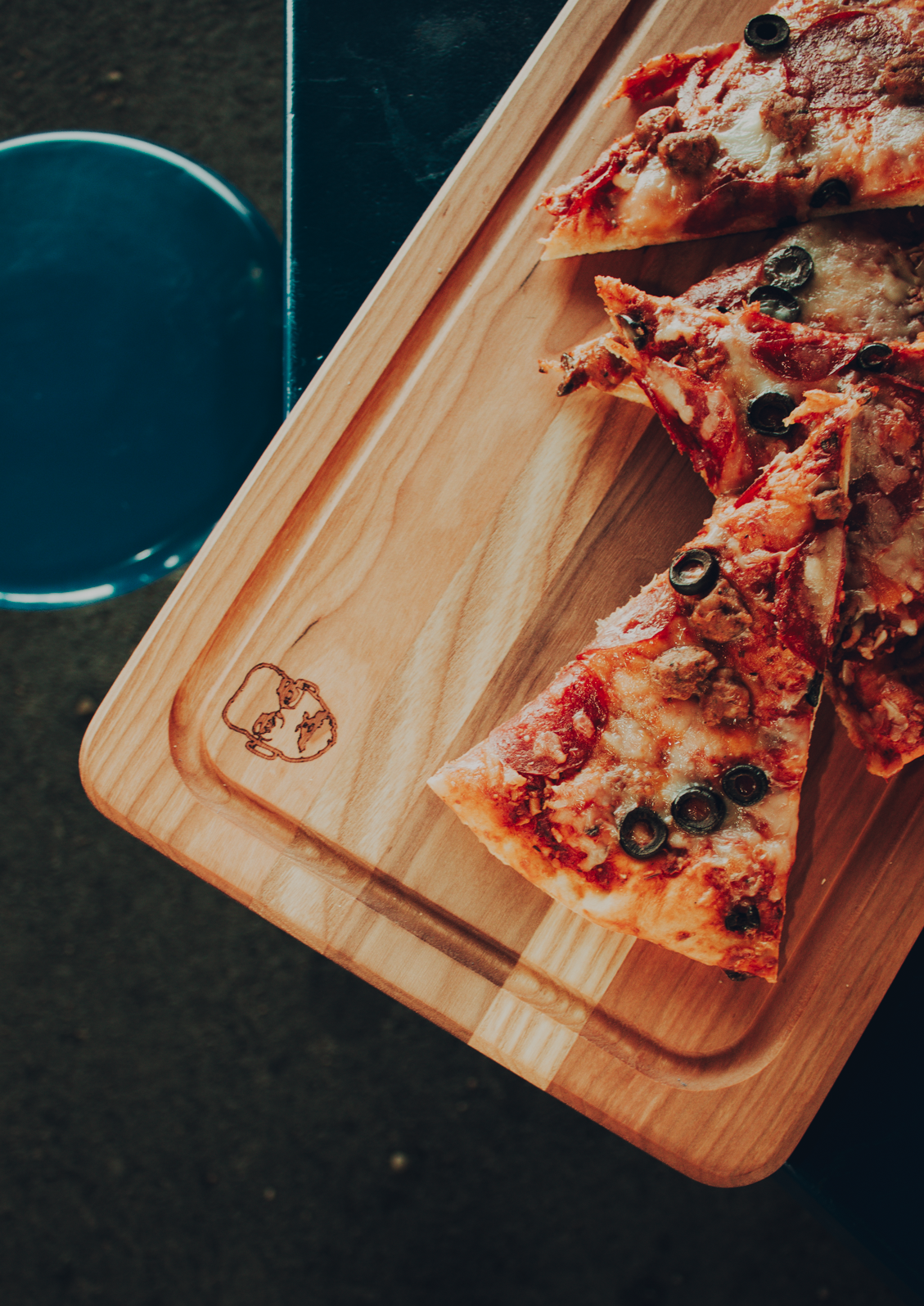 Pizza slices on a wooden cutting board with a Pizza John face engraved on it.
