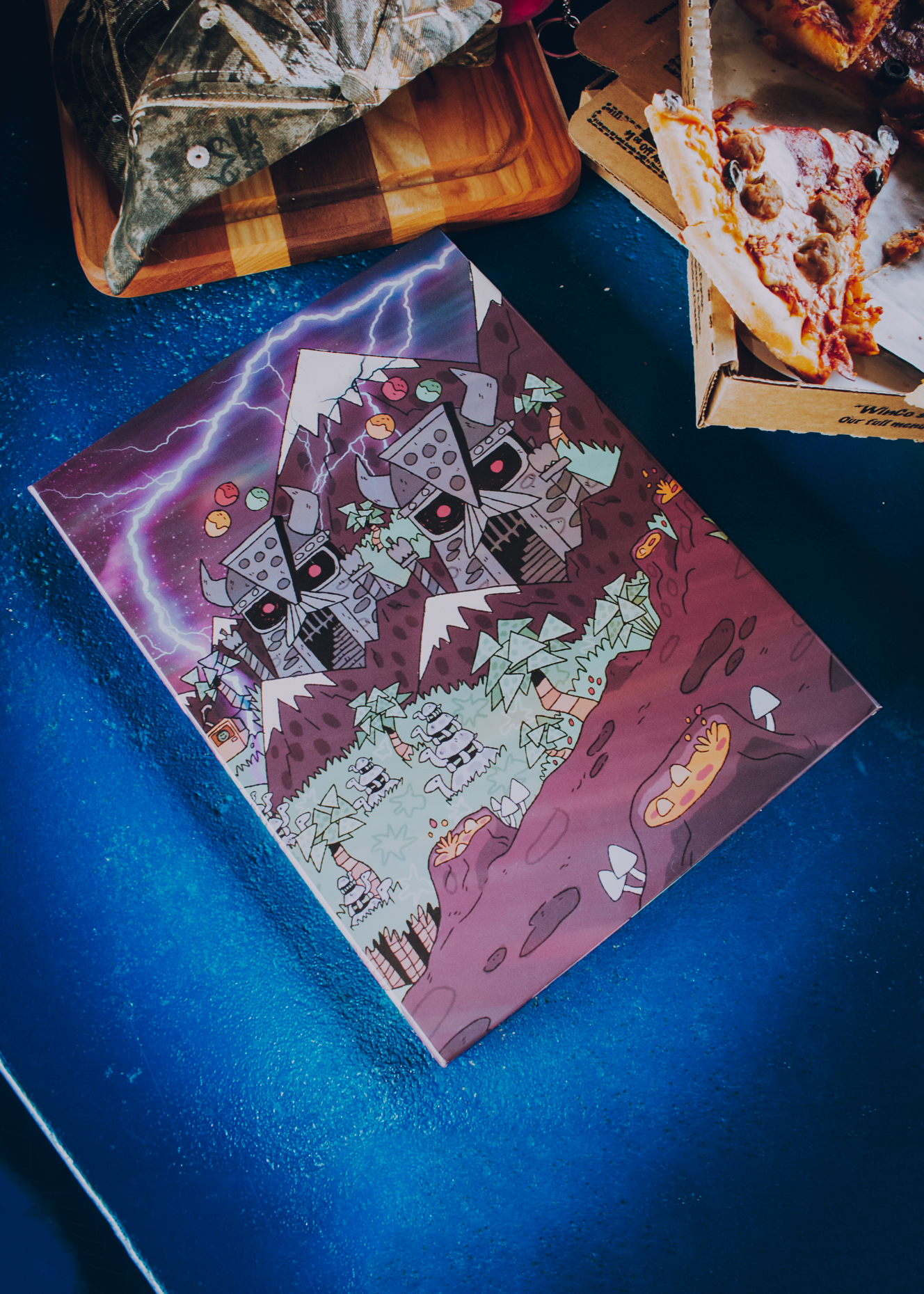 Colorful pizzamas-themed DM screen on a blue surface with pizza in the background