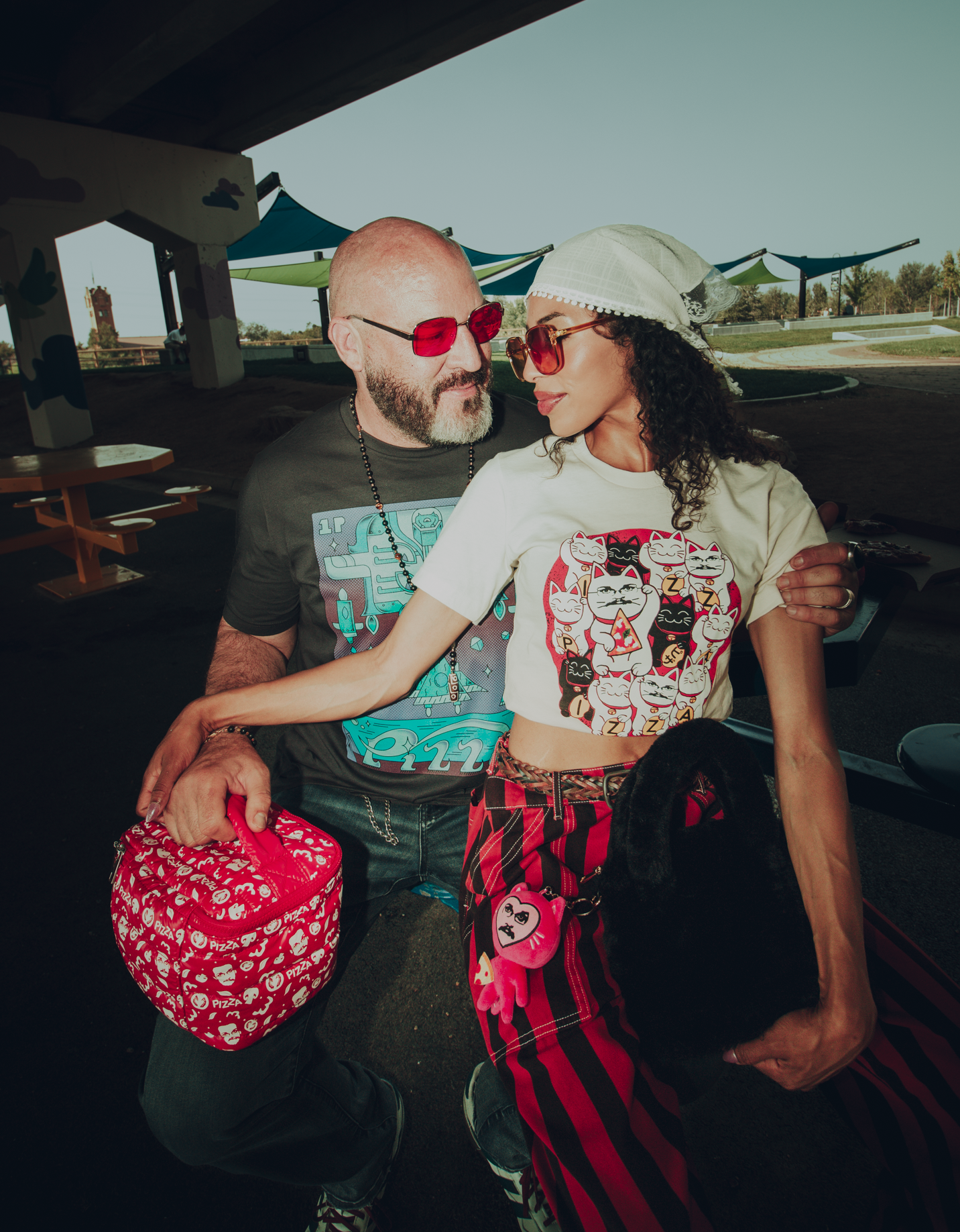Two people standing together outdoors, wearing sunglasses and Pizzamas shirts