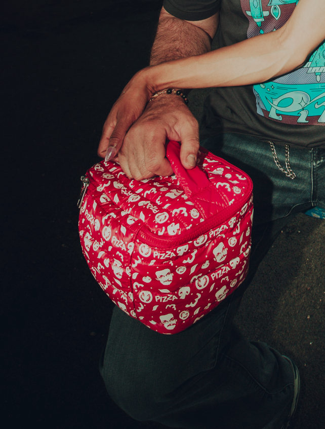Person holding a red puffy bag with white designs on a dark background