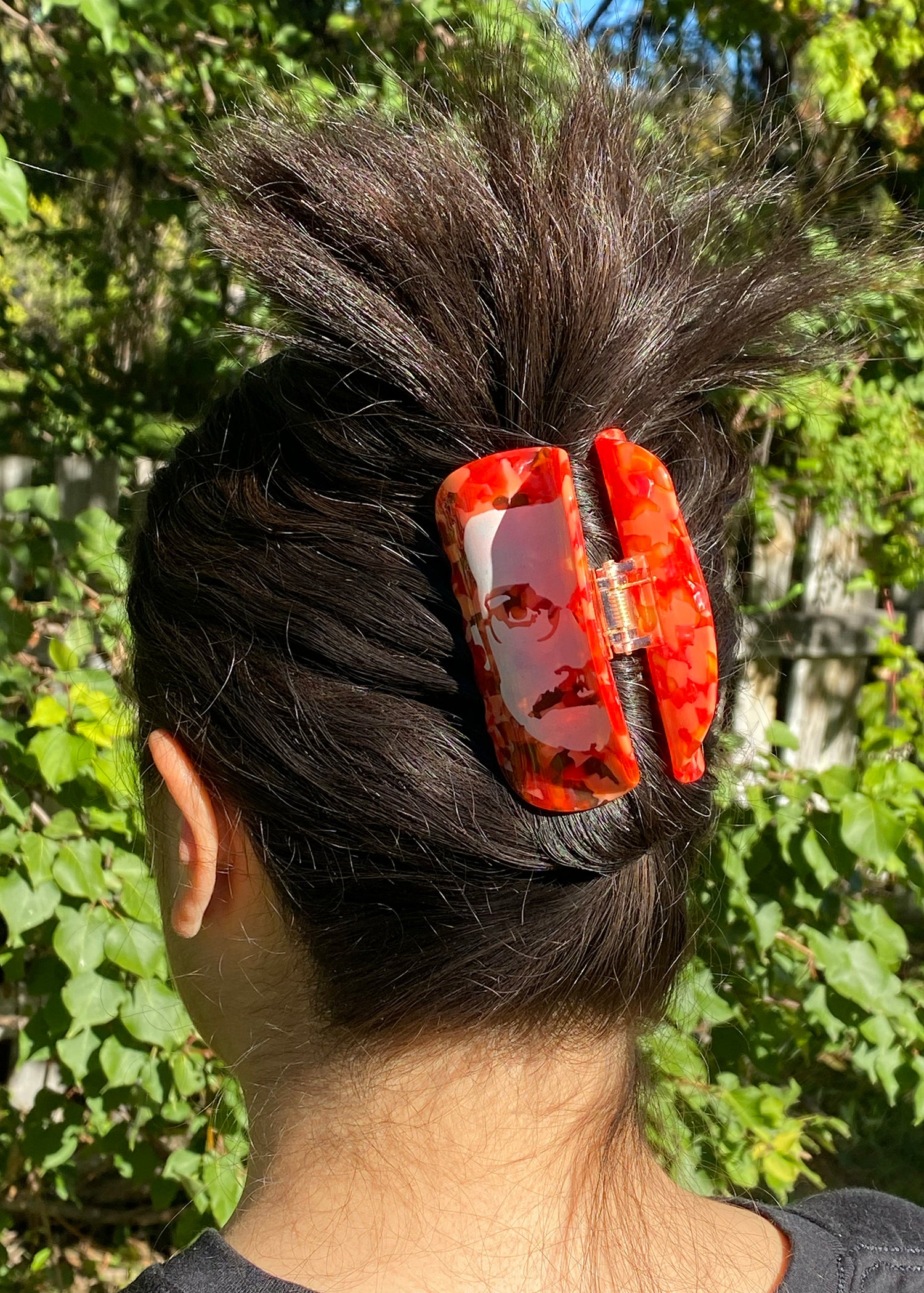 Person with a red hair clip in their hair against a green outdoor background