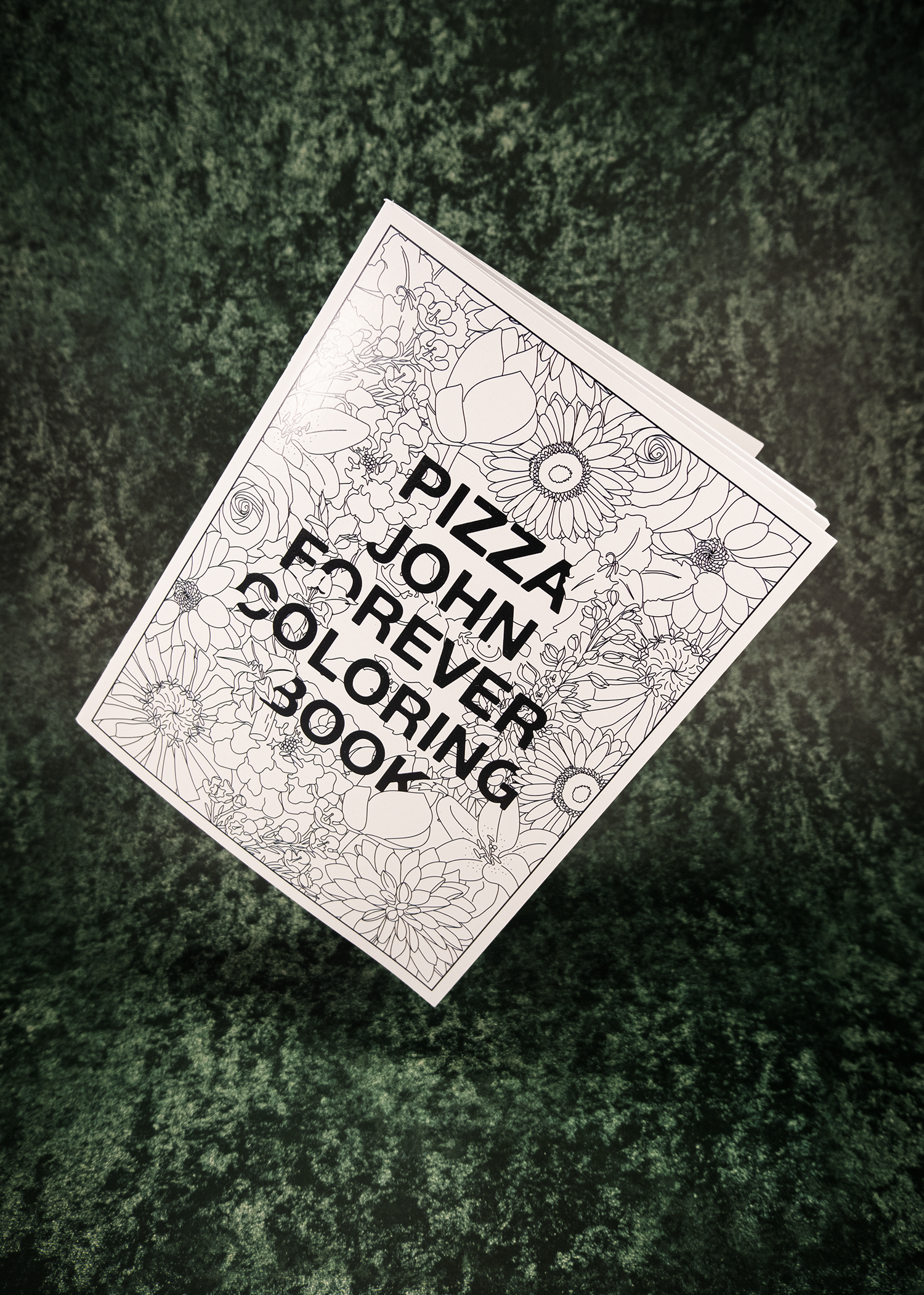 Coloring book titled 'Pizza John Forever Coloring Book' on a textured green surface