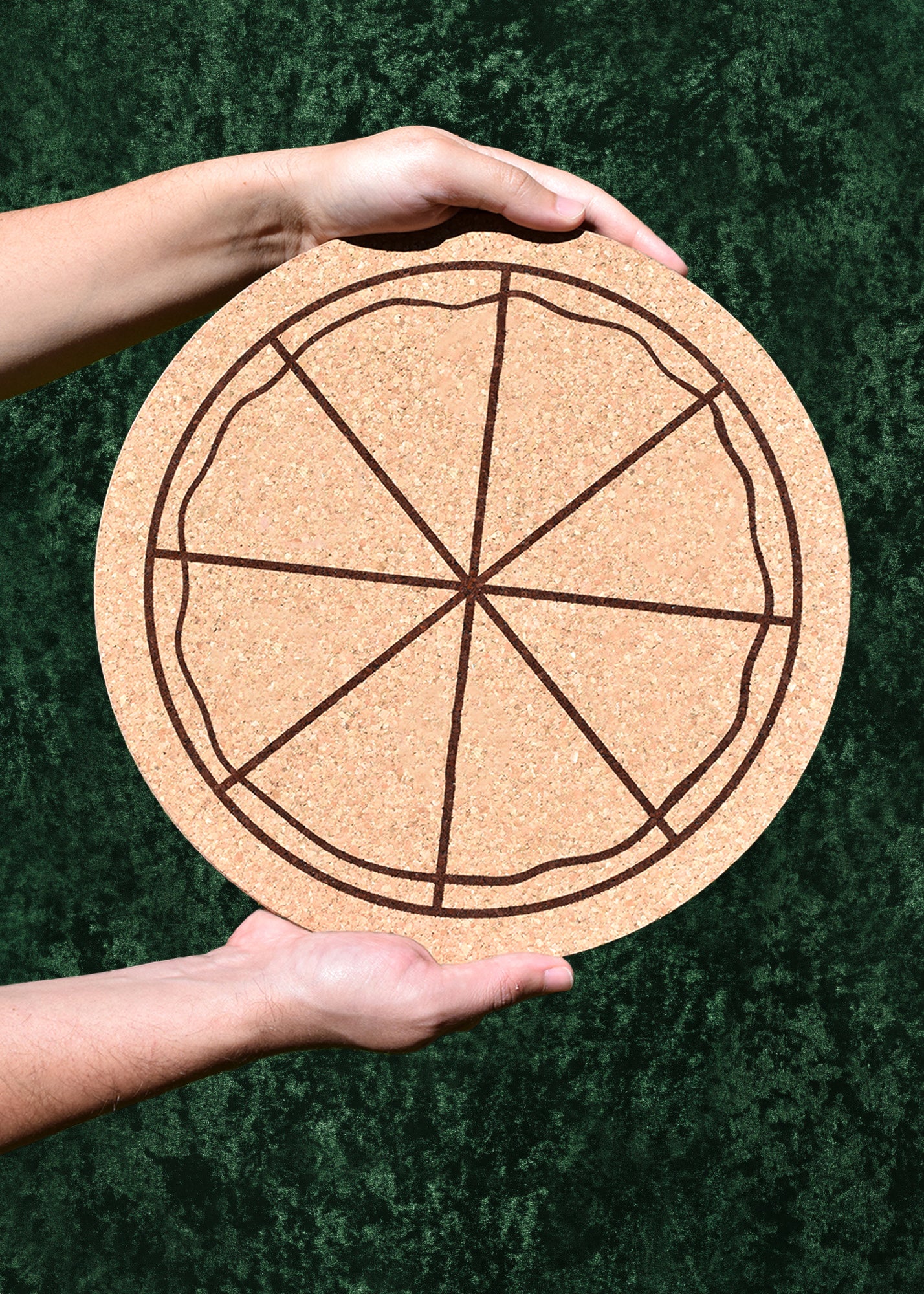 Corkboard with a pizza design held by a person against a green background