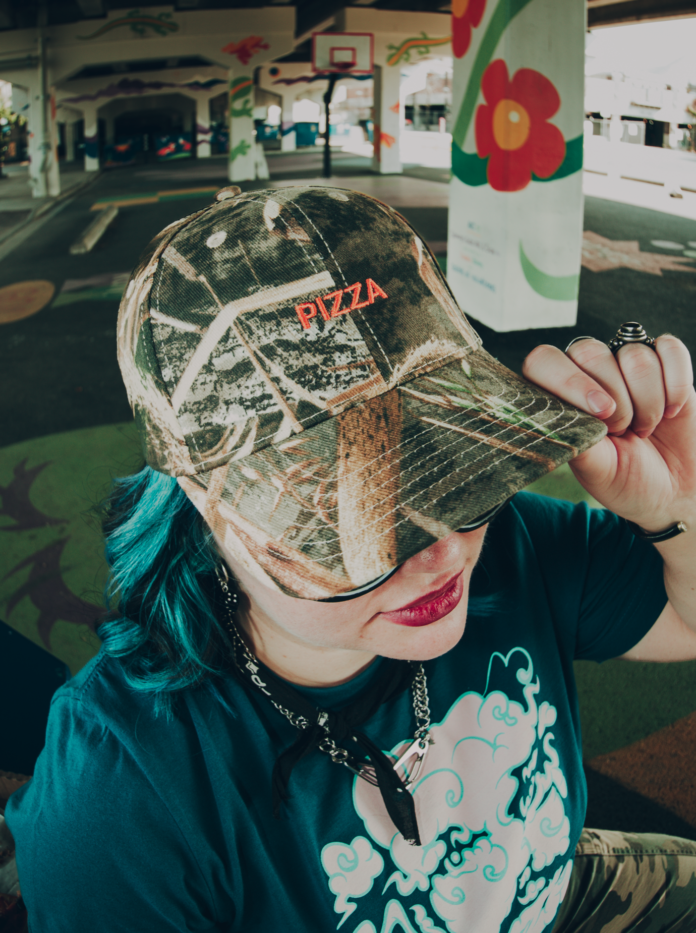 Person wearing a camouflage cap with 'PIZZA' text, in a colorful outdoor setting