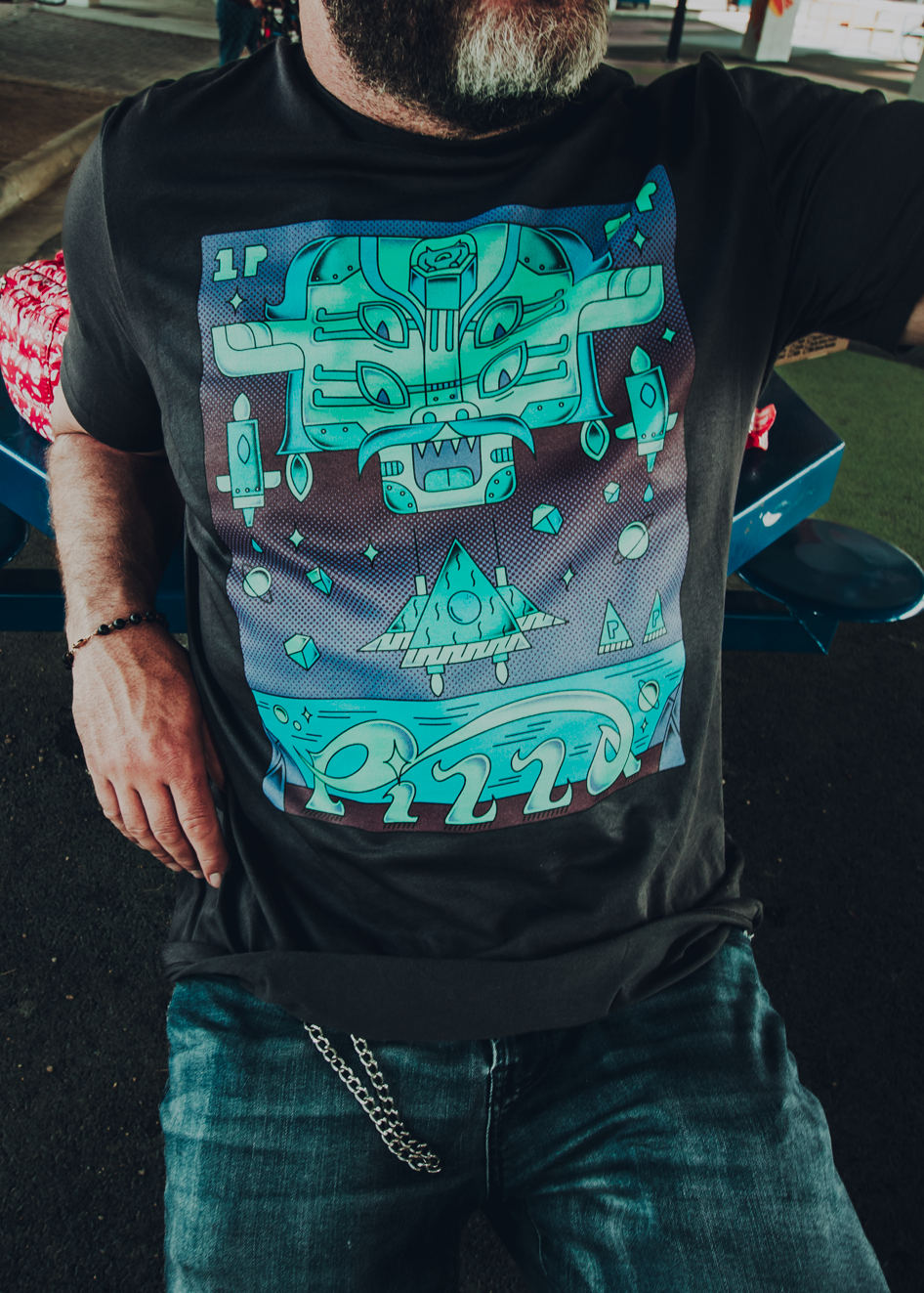 Person wearing a black t-shirt with a video-game themed Pizza John design in an outdoor setting