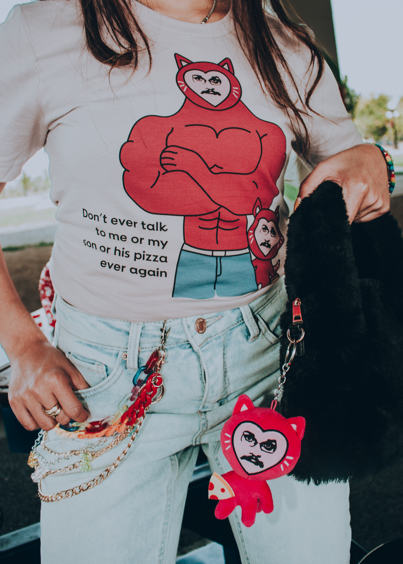 Person wearing a t-shirt with  Pizza John cat cartoon characters and text, wearing a matching keychain.