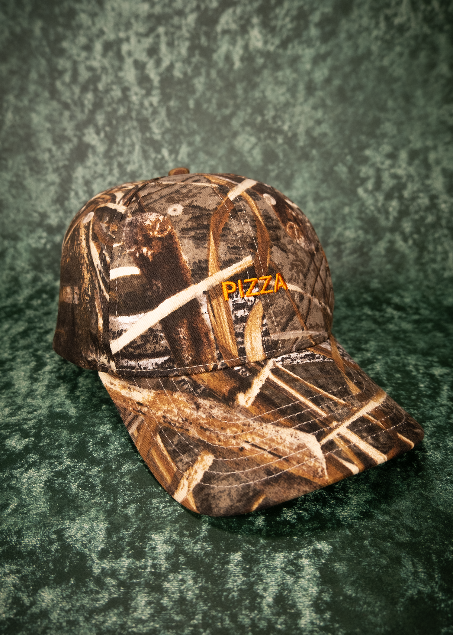 Camouflage-patterned cap with orange 'PIZZA' text on a textured green background